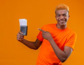 young-handsome-boy-wearing-orange-t-shirt-holding-air-ticket-pointing-it-with-finger-smiling-confident-standing-orange-wall_141793-22843
